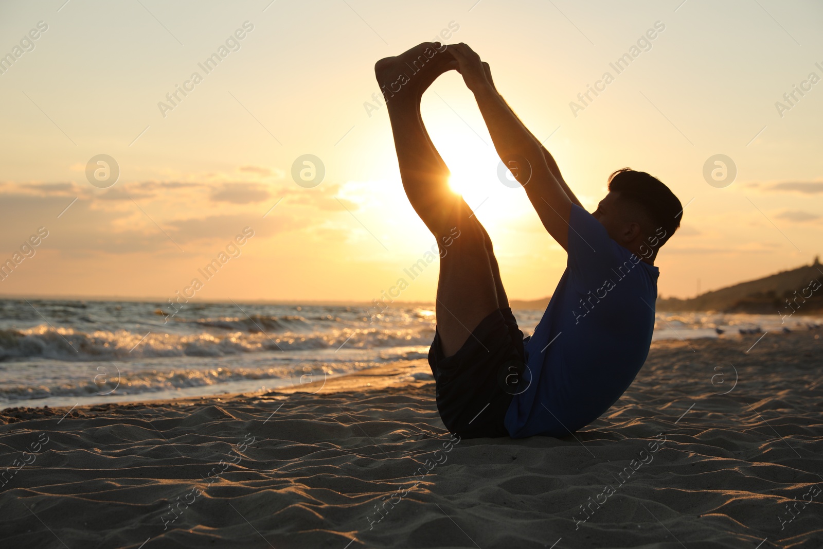 Photo of Sporty man doing exercise on sandy beach at sunset