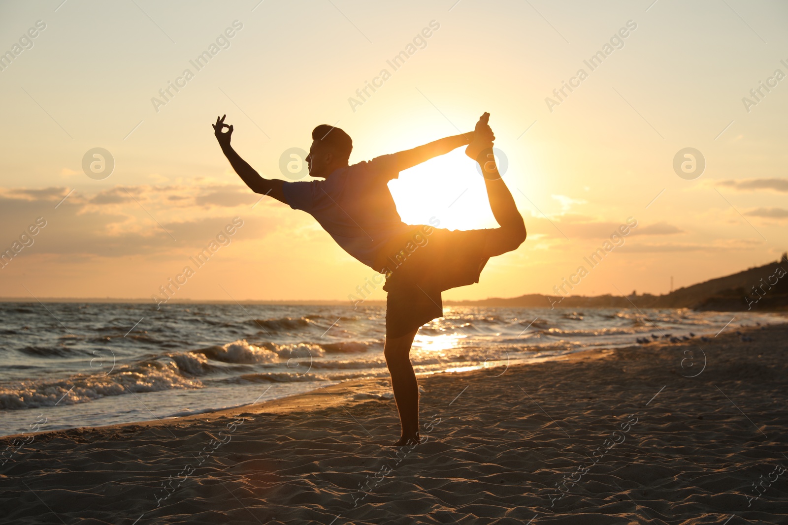 Photo of Sporty man doing exercise on sandy beach at sunset