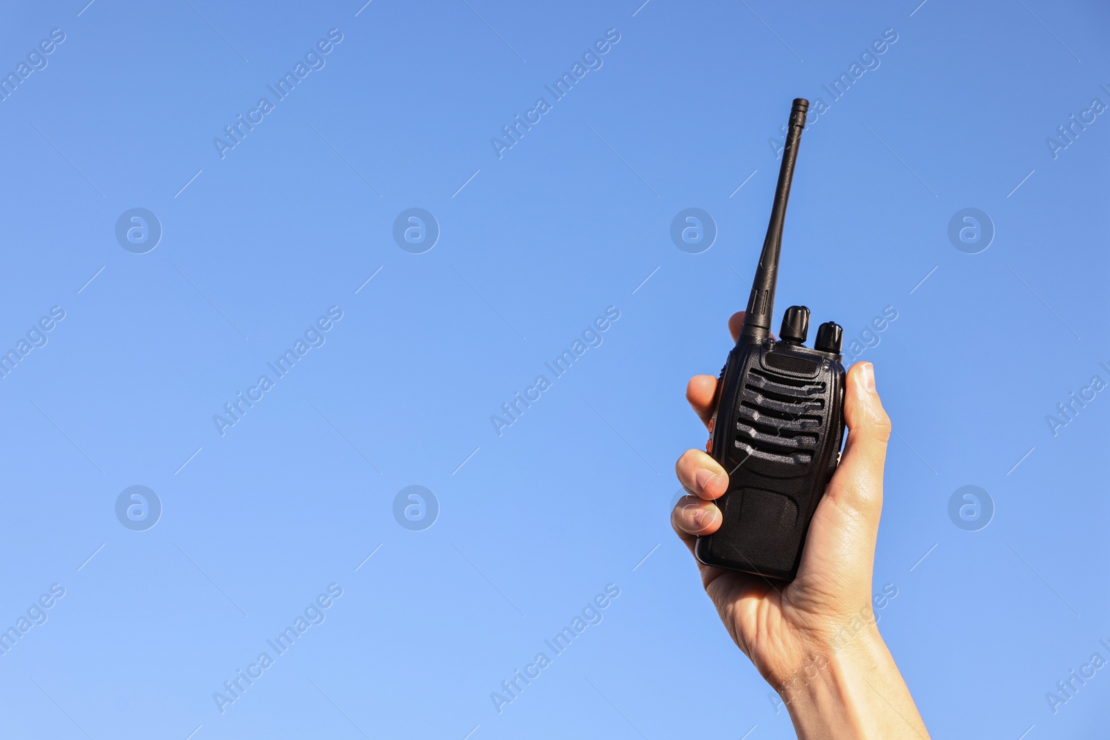 Photo of Woman with walkie talkie against blue sky outdoors, closeup. Space for text