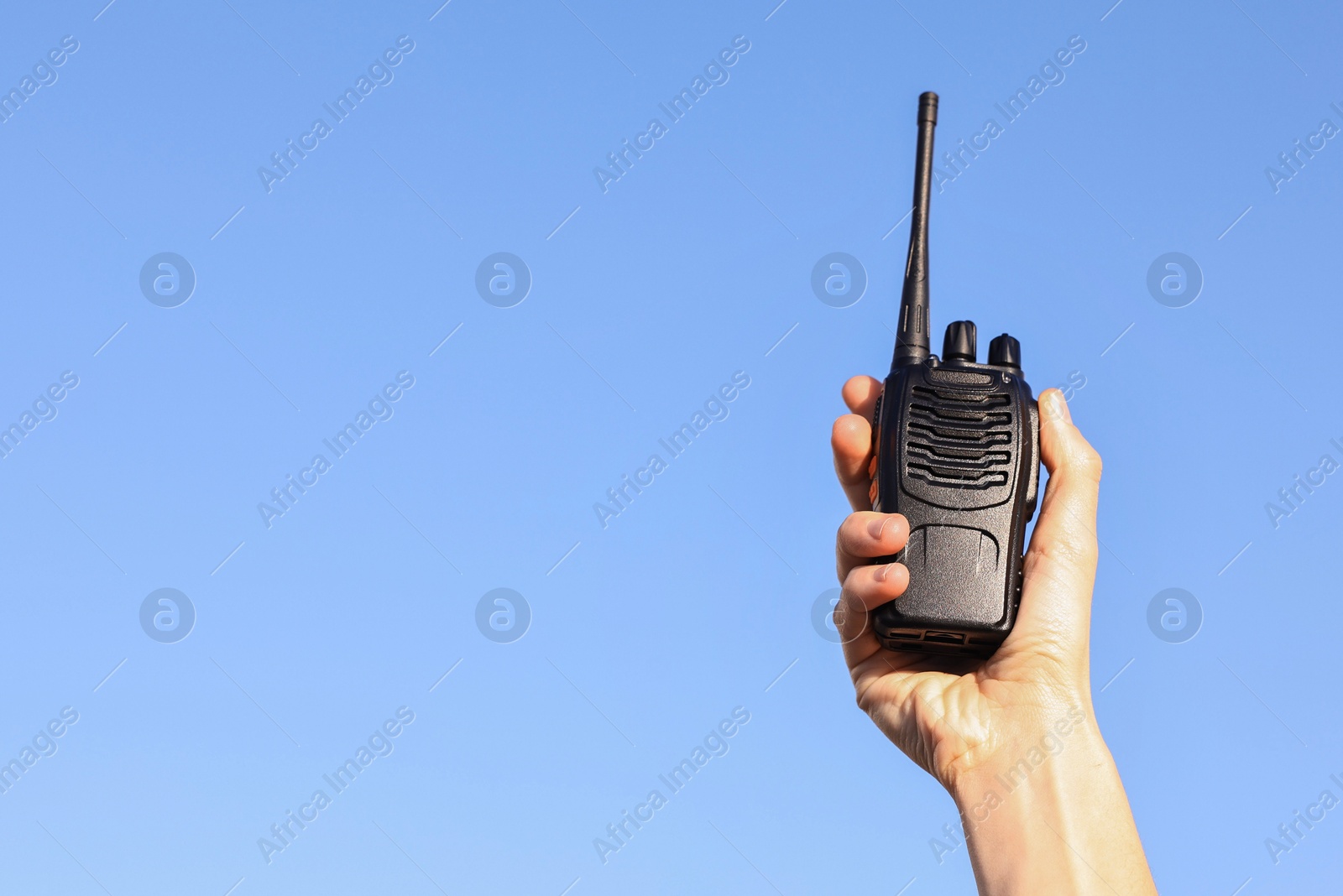 Photo of Woman with walkie talkie against blue sky outdoors, closeup. Space for text