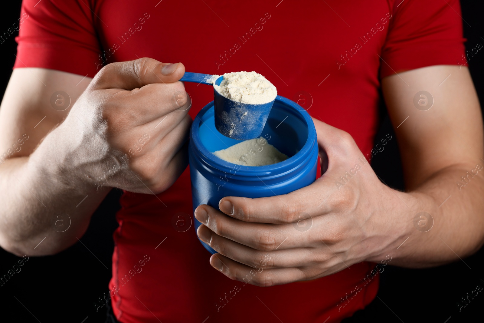 Photo of Sportsman taking protein with scoop on dark background, closeup