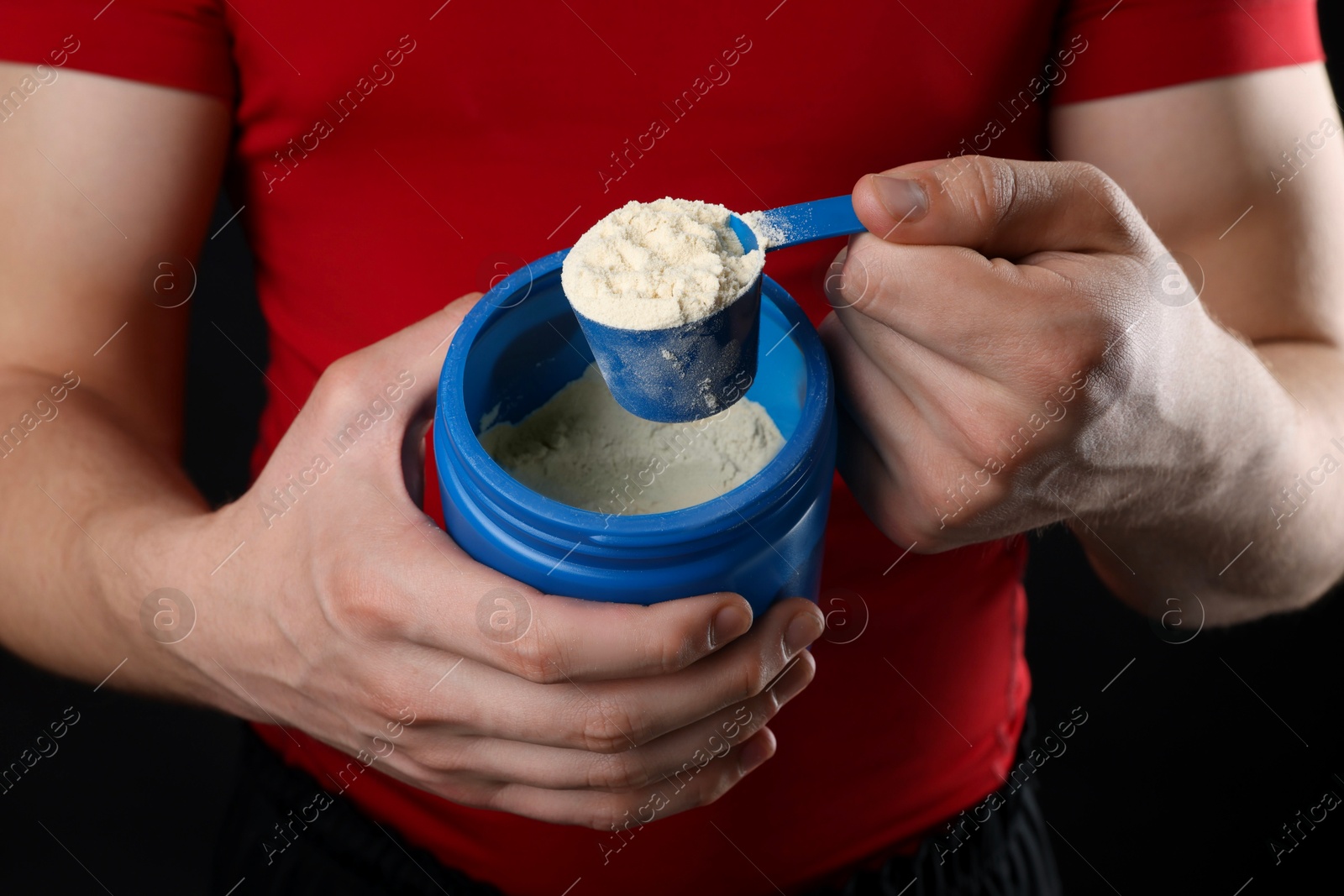 Photo of Sportsman taking protein with scoop on dark background, closeup