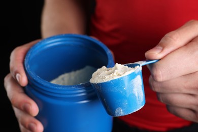 Photo of Sportsman taking protein with scoop on dark background, closeup