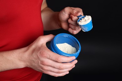 Sportsman taking protein with scoop on dark background, closeup