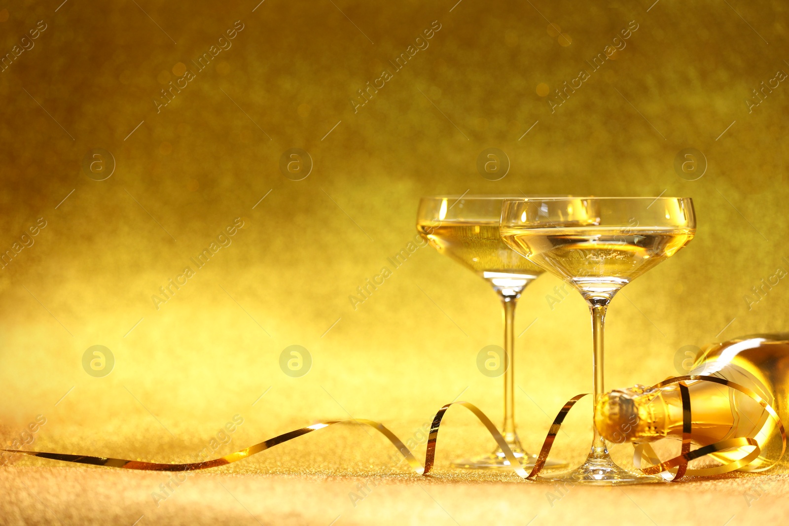 Photo of Champagne in glasses and bottle on golden background. Space for text