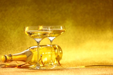 Photo of Champagne in glasses and bottle on golden background. Space for text