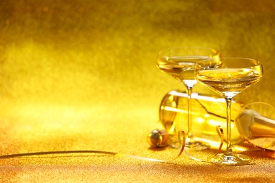 Photo of Champagne in glasses and bottle on golden background. Space for text