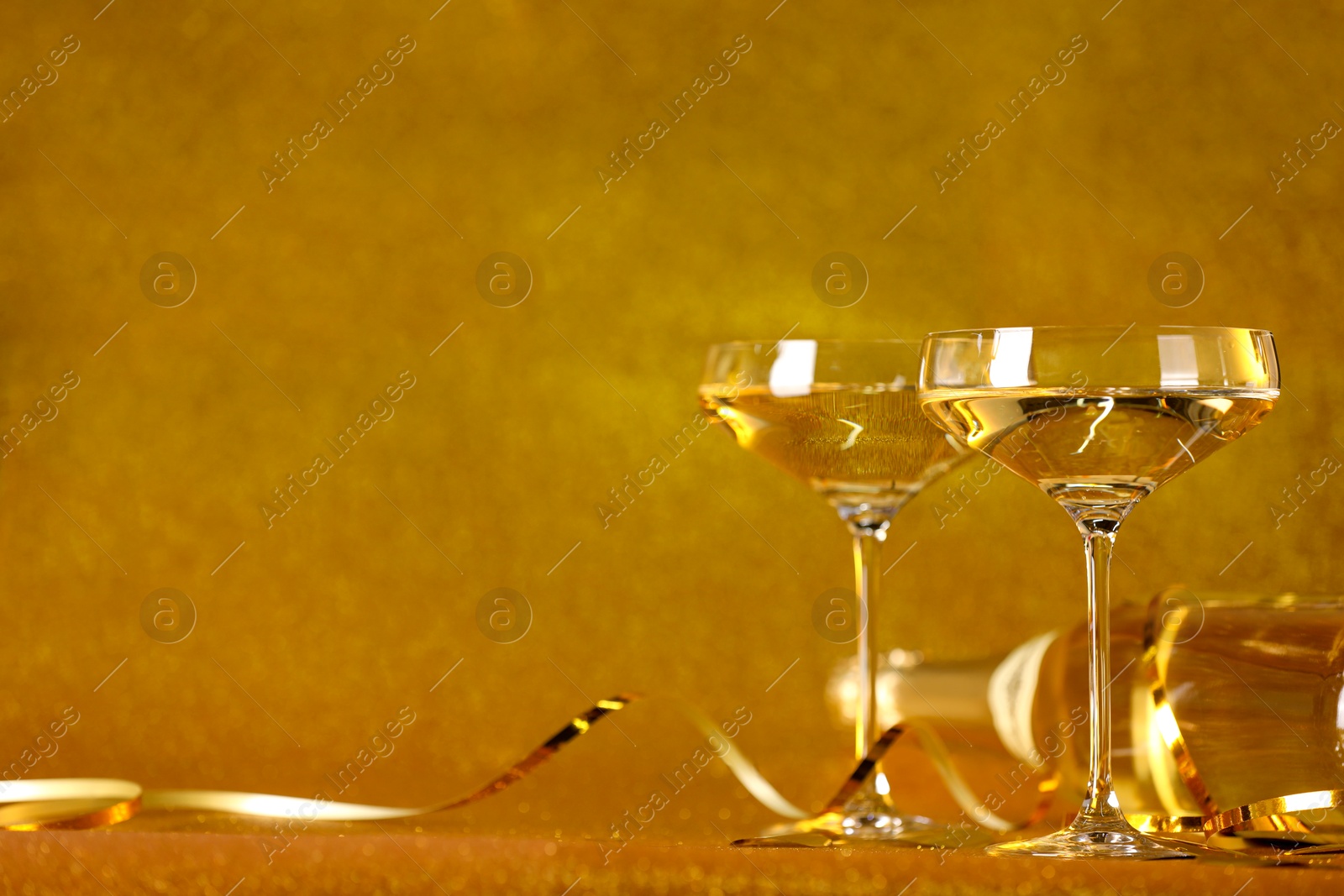 Photo of Champagne in glasses and bottle on golden background. Space for text