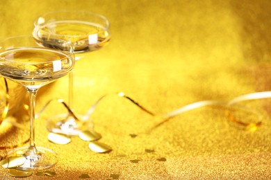 Photo of Champagne in glasses, confetti and streamers on golden background. Space for text