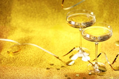 Photo of Champagne in glasses, confetti and streamers on golden background. Space for text