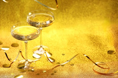 Photo of Champagne in glasses, confetti and streamers on golden background. Space for text