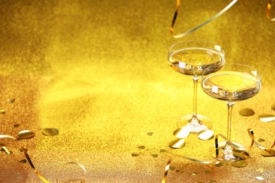 Photo of Champagne in glasses, confetti and streamers on golden background. Space for text