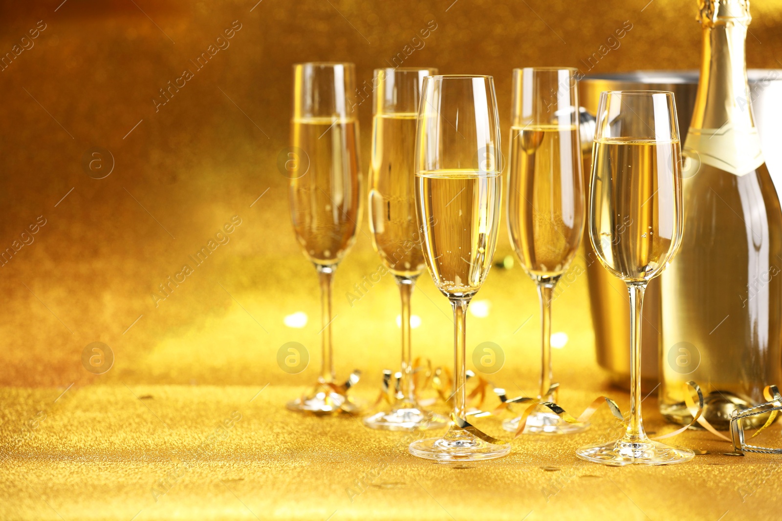 Photo of Champagne, bottle, ice bucket and streamers on golden background. Space for text