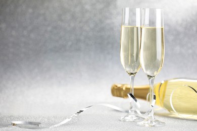 Photo of Champagne in glasses and bottle on silver background. Space for text