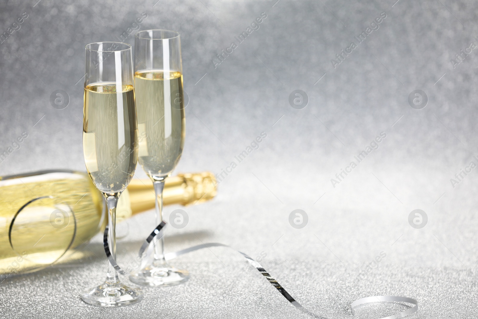 Photo of Champagne in glasses and bottle on silver background. Space for text