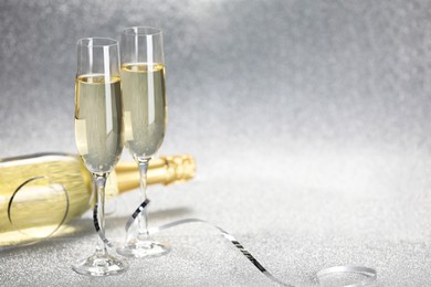 Photo of Champagne in glasses and bottle on silver background. Space for text