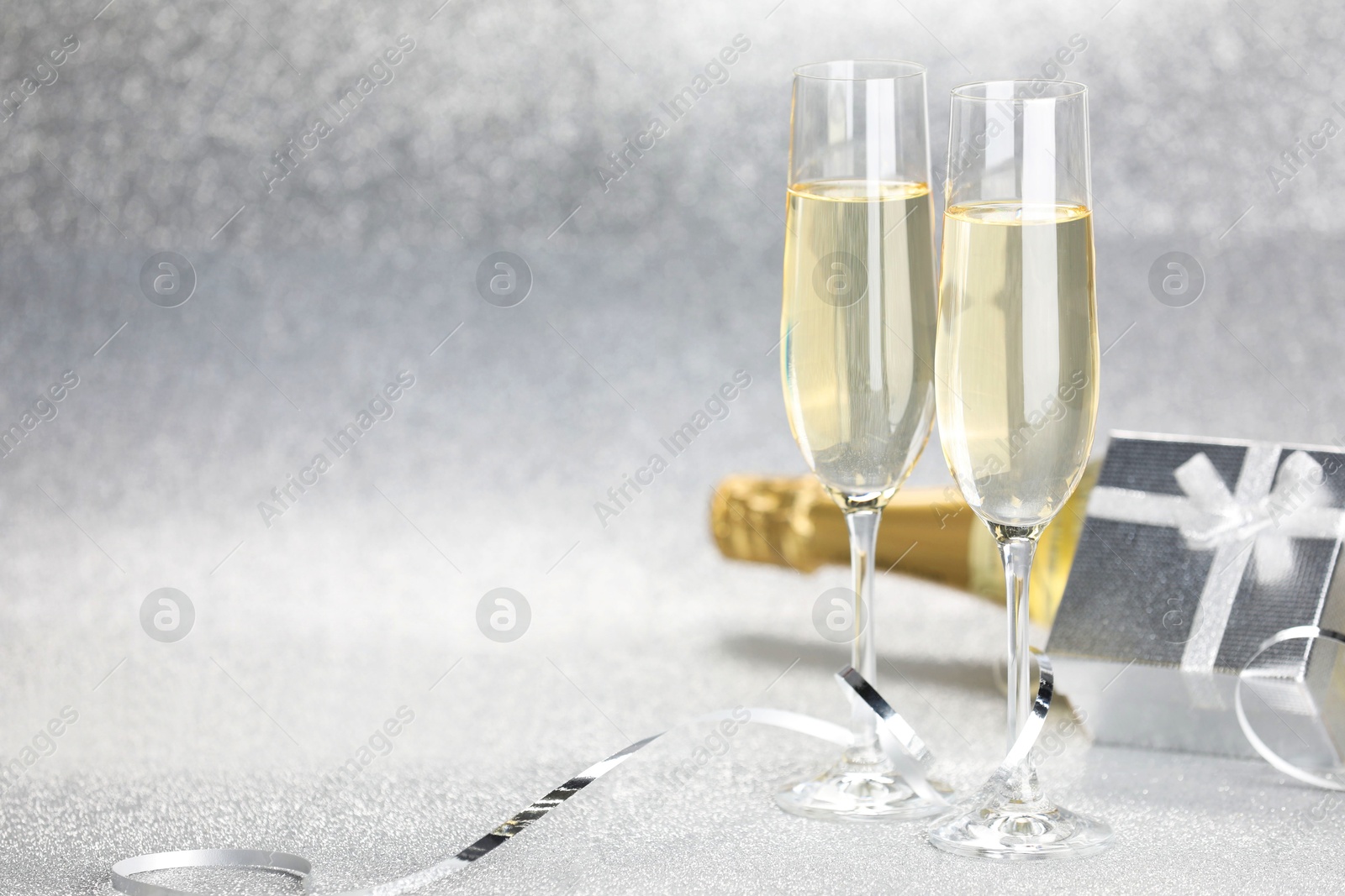 Photo of Champagne in glasses, bottle, gift box and streamers on silver background. Space for text