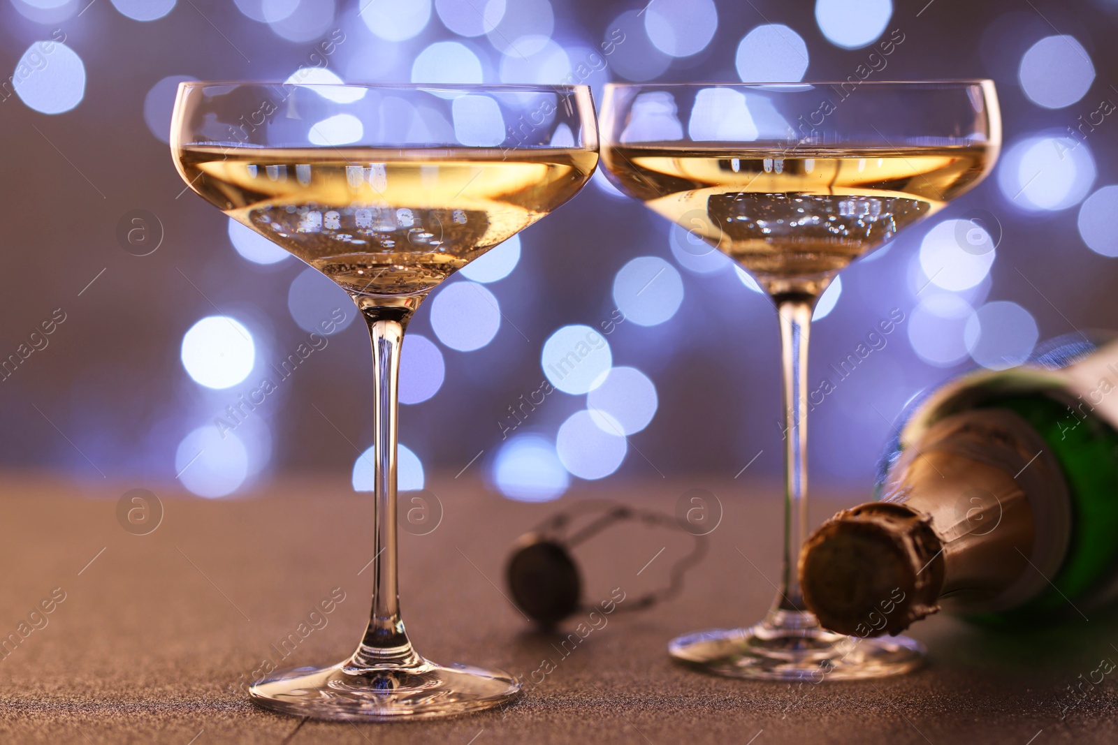 Photo of Champagne in glasses and bottle on table against blurred lights, closeup