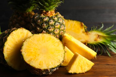 Photo of Whole and cut ripe pineapples on wooden table, closeup