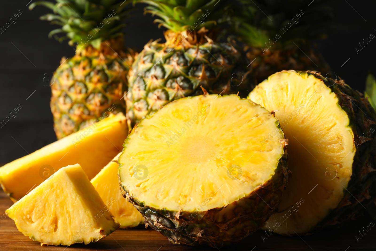 Photo of Whole and cut ripe pineapples on wooden table, closeup