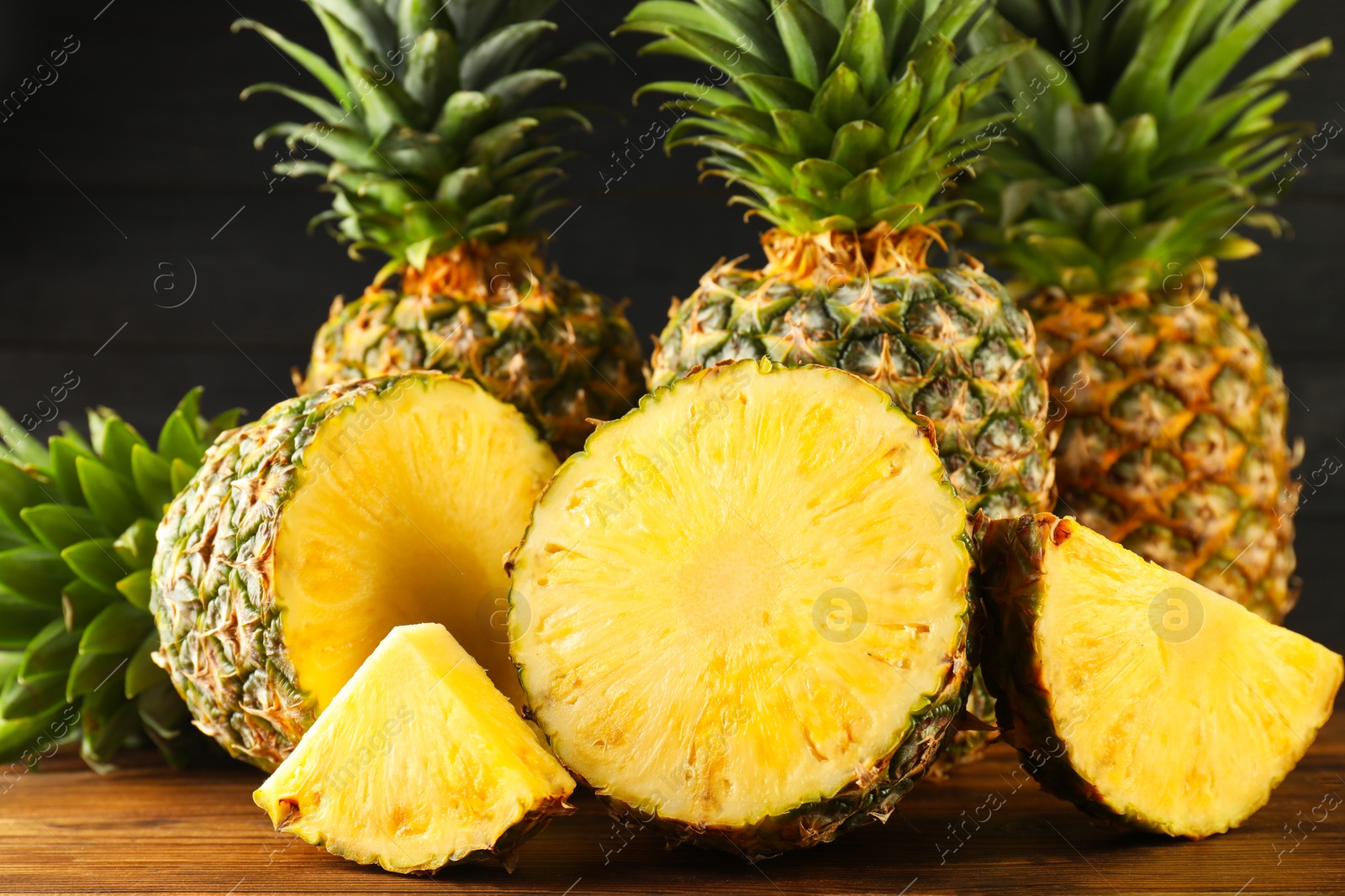 Photo of Whole and cut ripe pineapples on wooden table