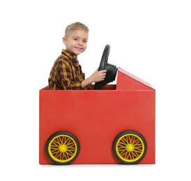 Photo of Little boy driving car made of cardboard on white background