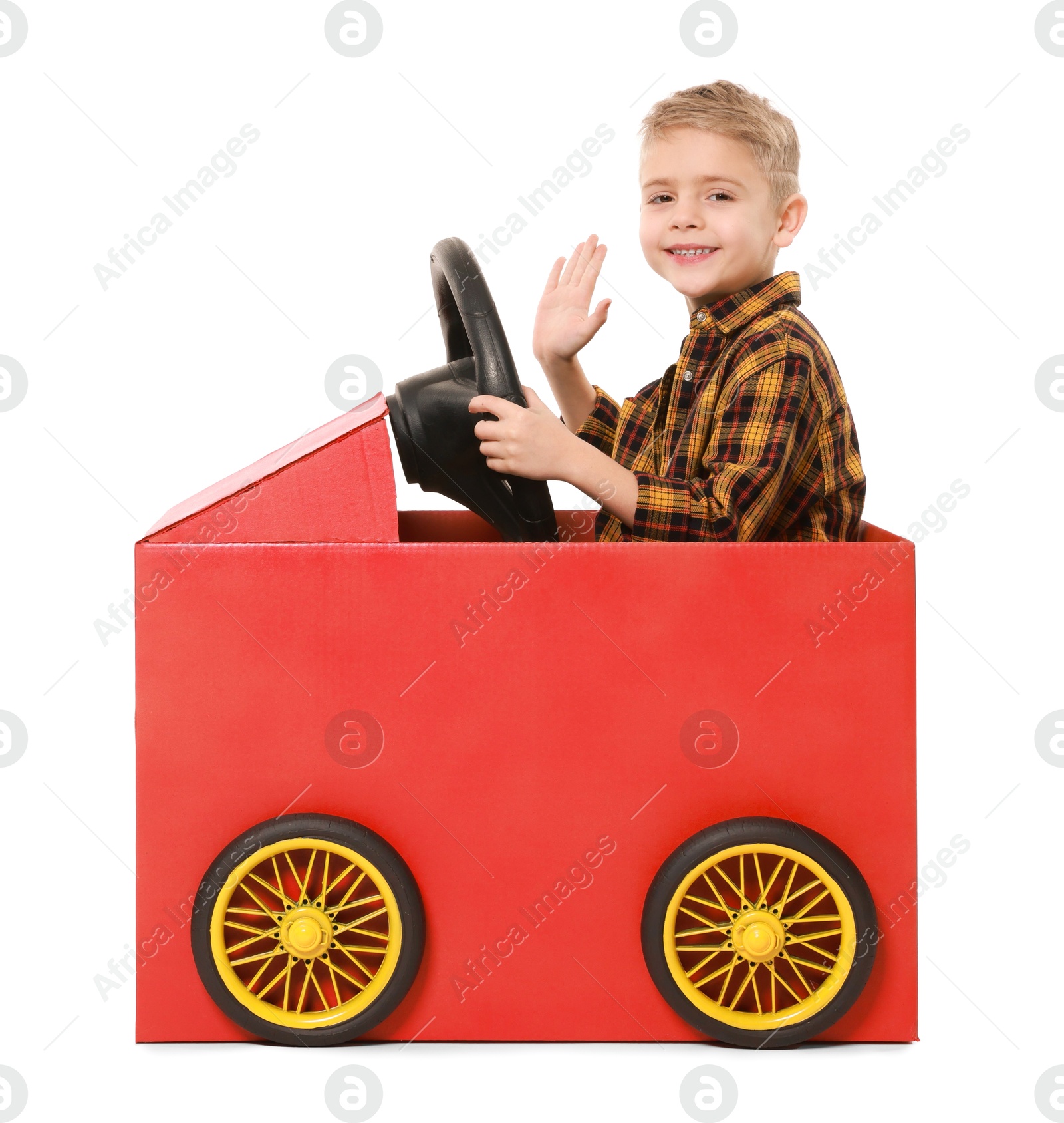 Photo of Little boy waving while driving car made of cardboard on white background