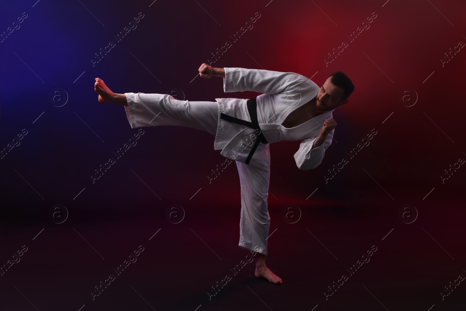 Photo of Man wearing uniform practicing karate in color lights against black background