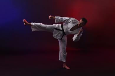 Photo of Man wearing uniform practicing karate in color lights against black background