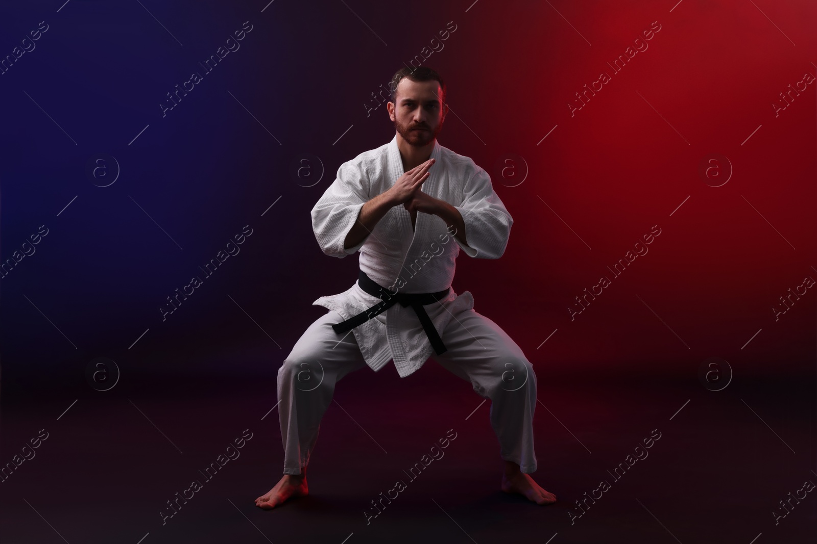 Photo of Man wearing uniform practicing karate in color lights against black background