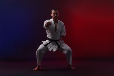 Photo of Man wearing uniform practicing karate in color lights against black background