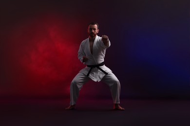 Photo of Man wearing uniform practicing karate in color lights against black background