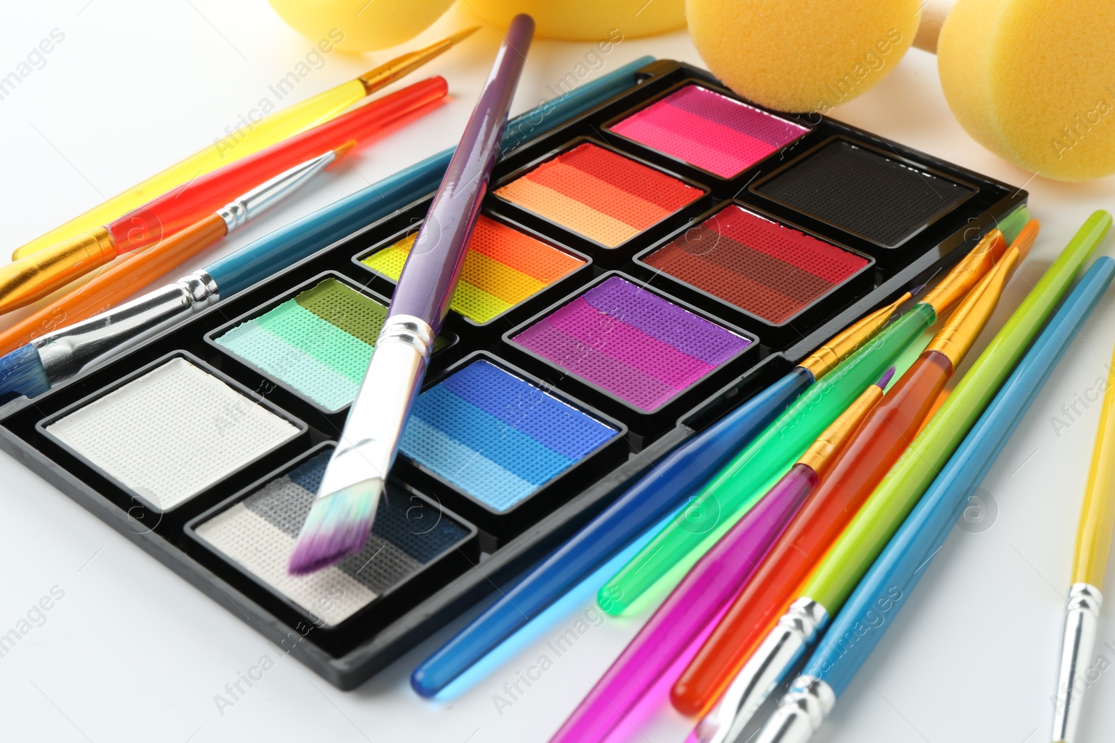 Photo of Bright face paint palette, brushes and sponges on white background, closeup