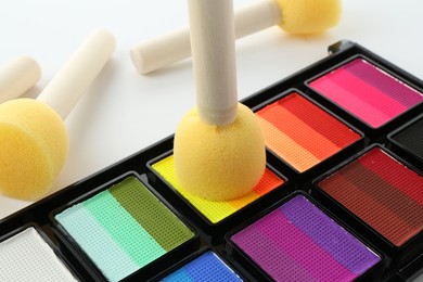 Photo of Bright face paint palette and sponges on white background, closeup