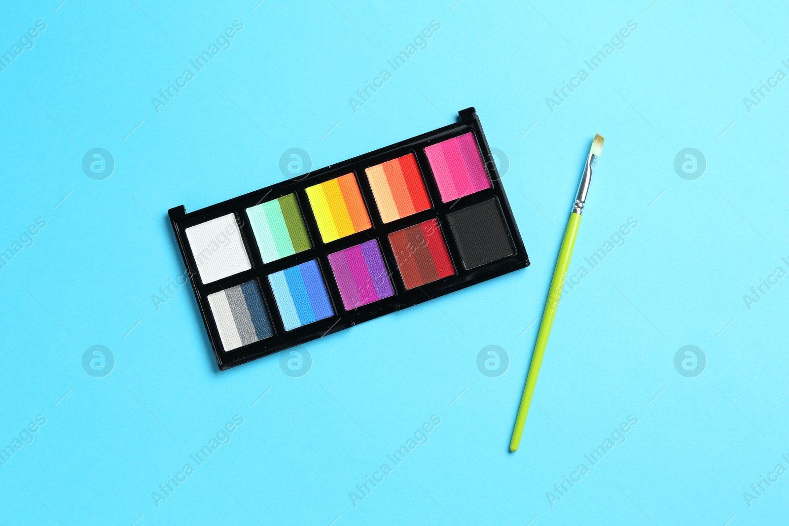 Photo of Bright face paints and brush on light blue background, top view