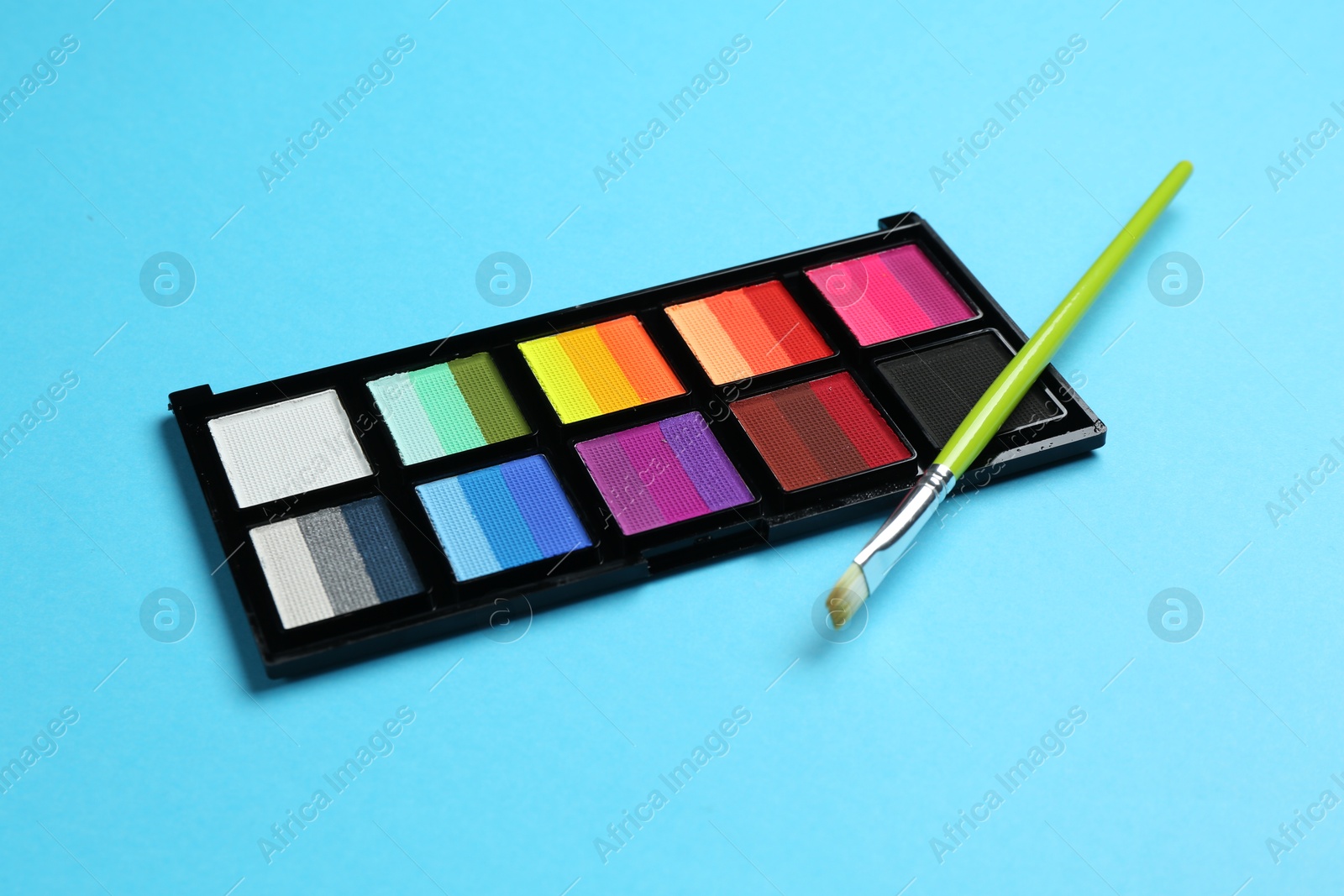 Photo of Bright face paints and brush on light blue background