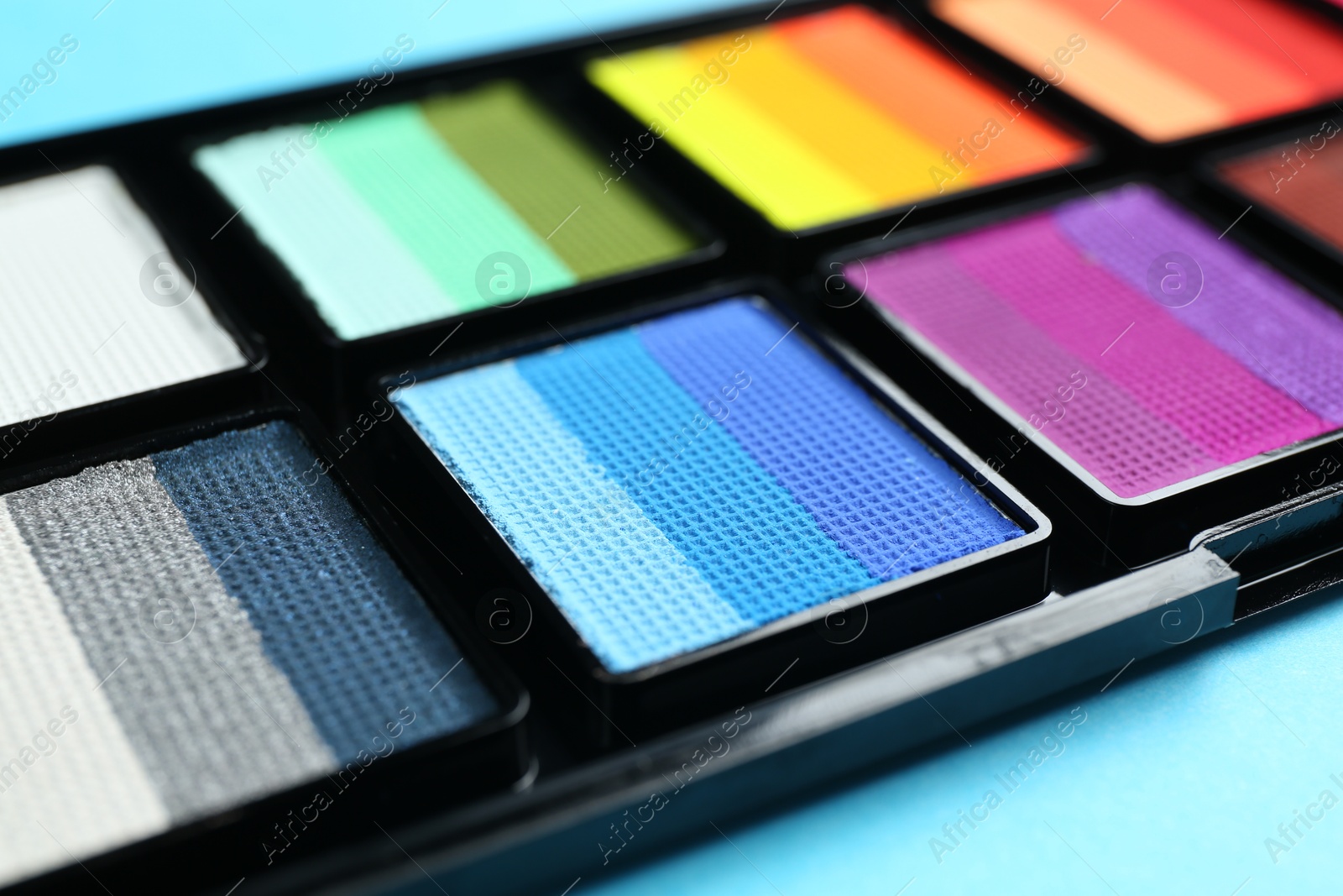 Photo of Bright face paints on light blue background, closeup