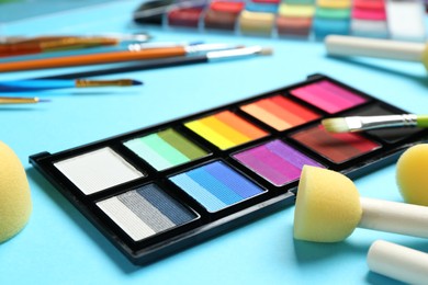 Photo of Bright face paints, brushes and sponges on light blue background, closeup