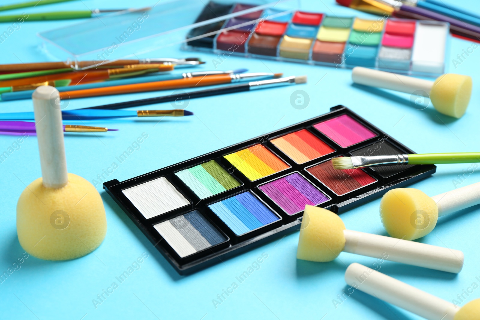 Photo of Bright face paints, brushes and sponges on light blue background