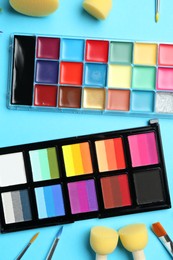 Photo of Bright face paints, brushes and sponges on light blue background, flat lay