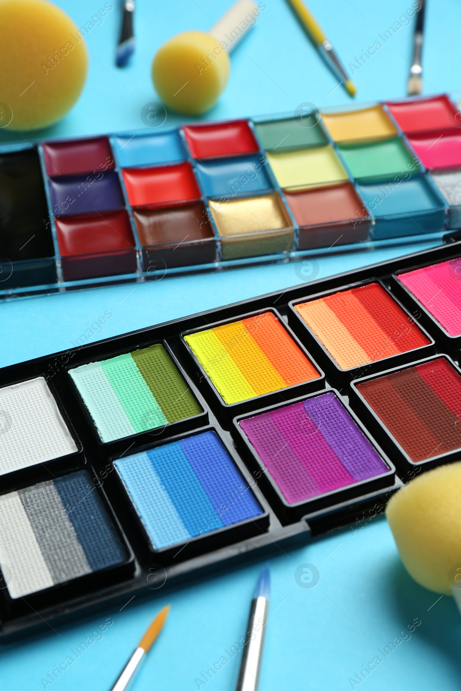 Photo of Bright face paints, brushes and sponges on light blue background, closeup