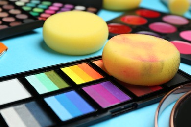 Photo of Bright face paints and sponges on light blue background, closeup