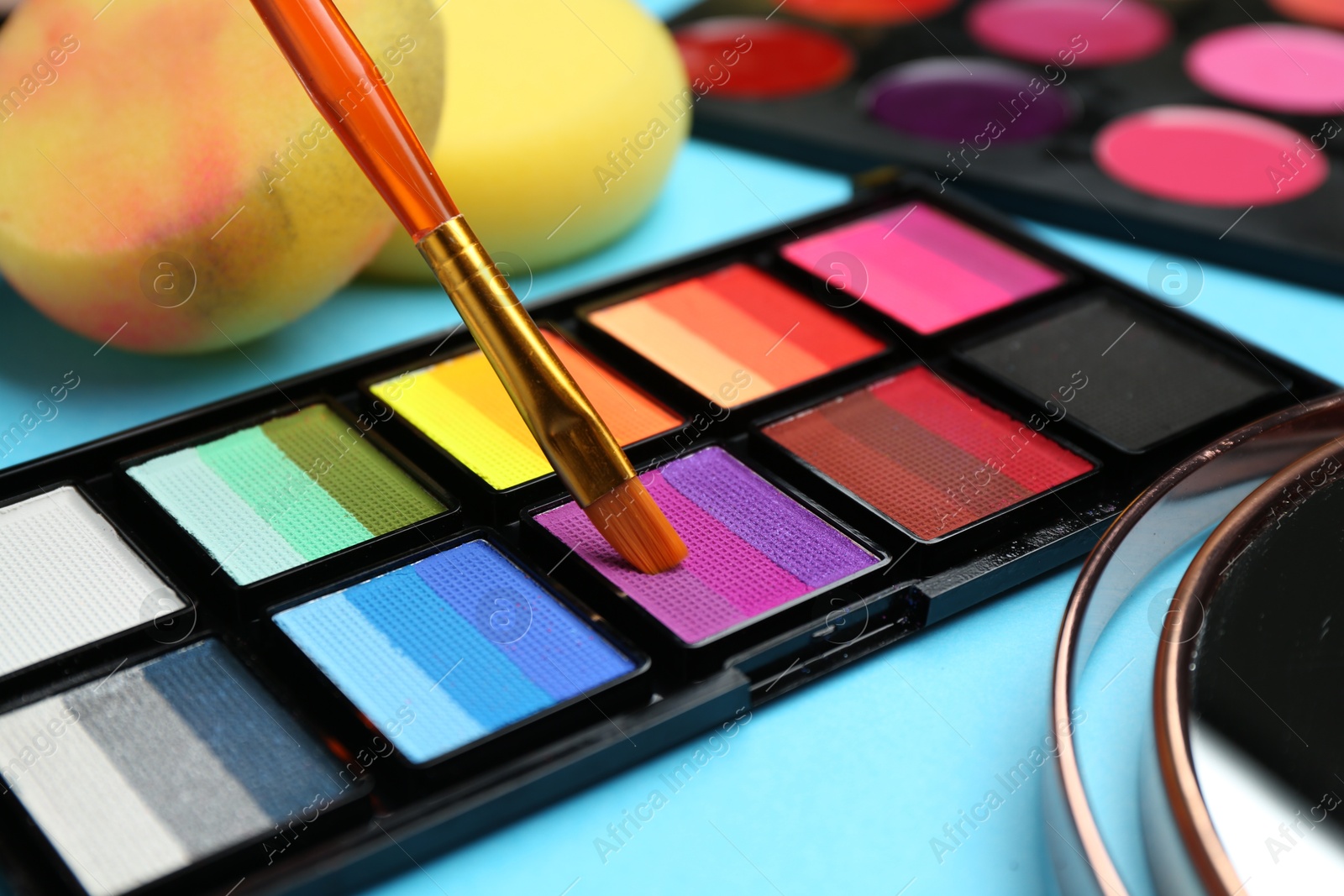 Photo of Taking face paint with brush from palette on light blue background, closeup