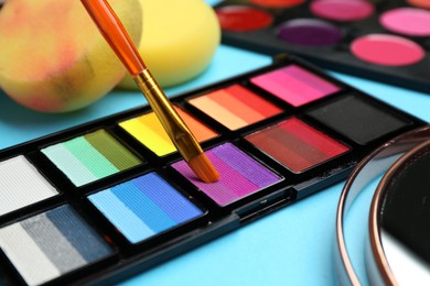 Photo of Taking face paint with brush from palette on light blue background, closeup