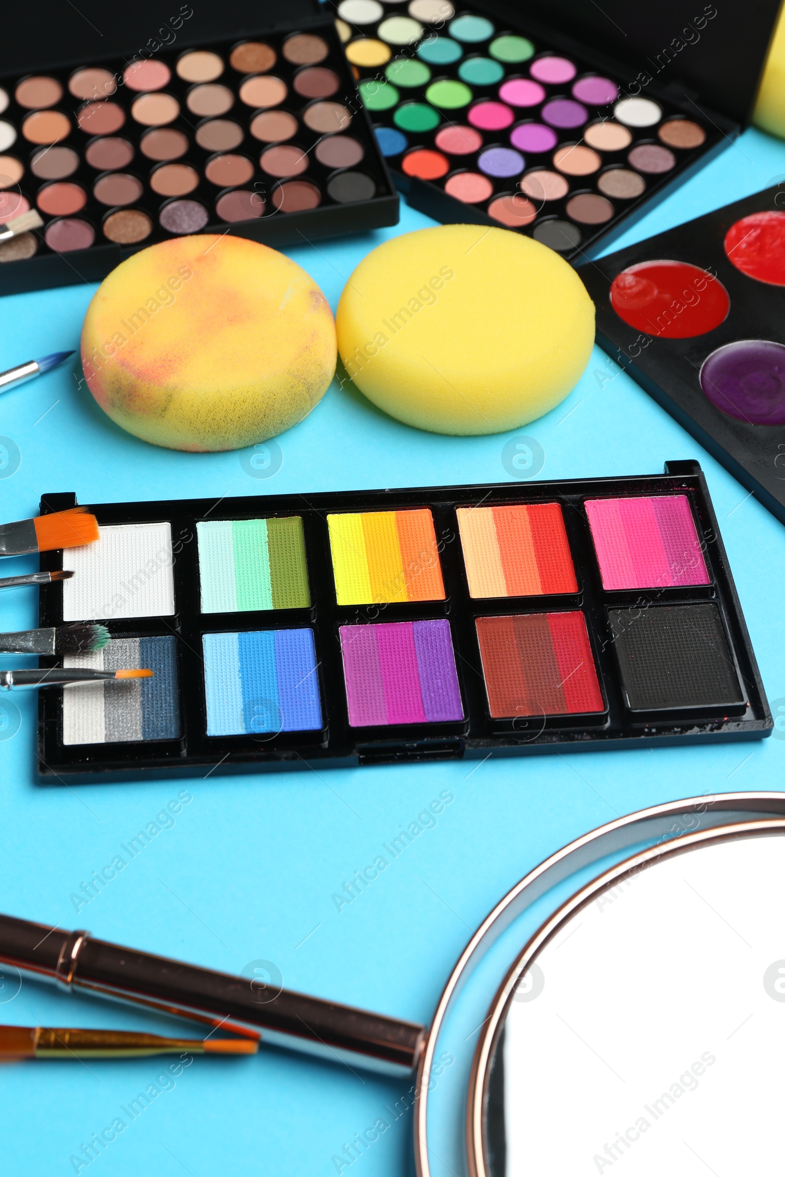 Photo of Bright face paints, brushes, mirror and sponges on light blue background