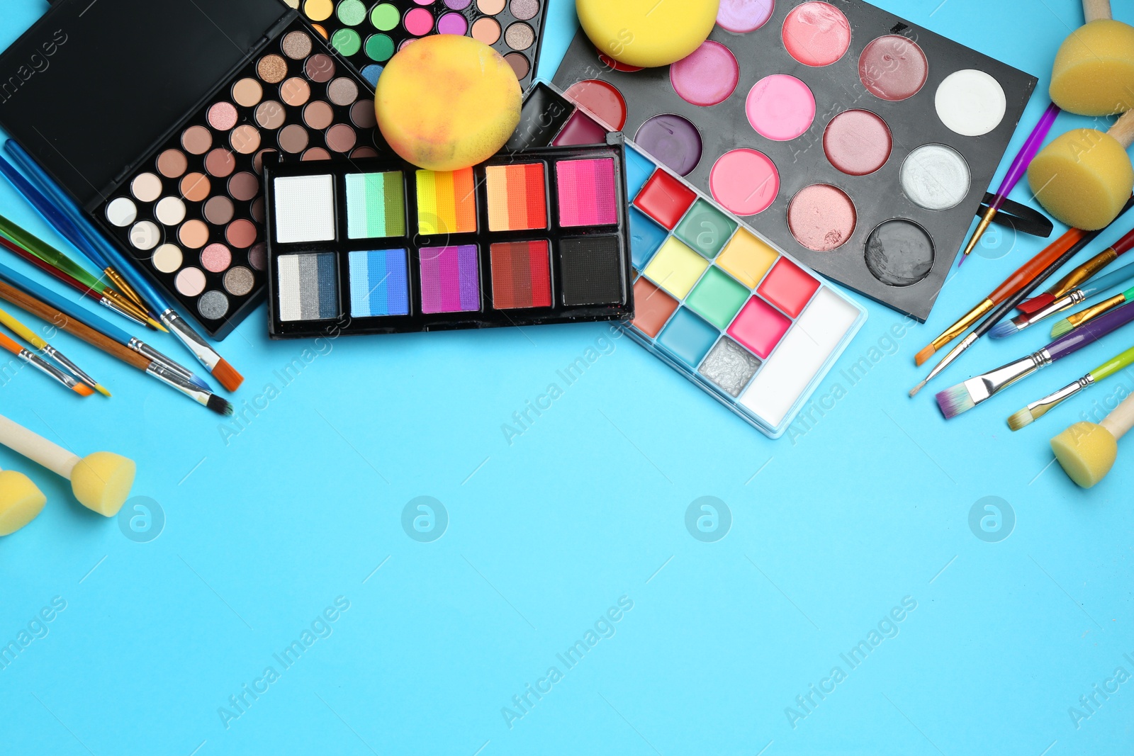 Photo of Bright face paints, brushes and sponges on light blue background, flat lay. Space for text