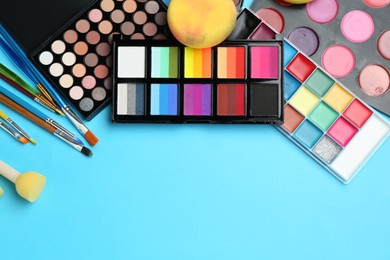 Photo of Bright face paints, brushes and sponges on light blue background, flat lay. Space for text