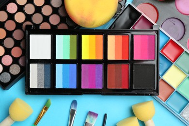 Photo of Bright face paints, brushes and sponges on light blue background, flat lay