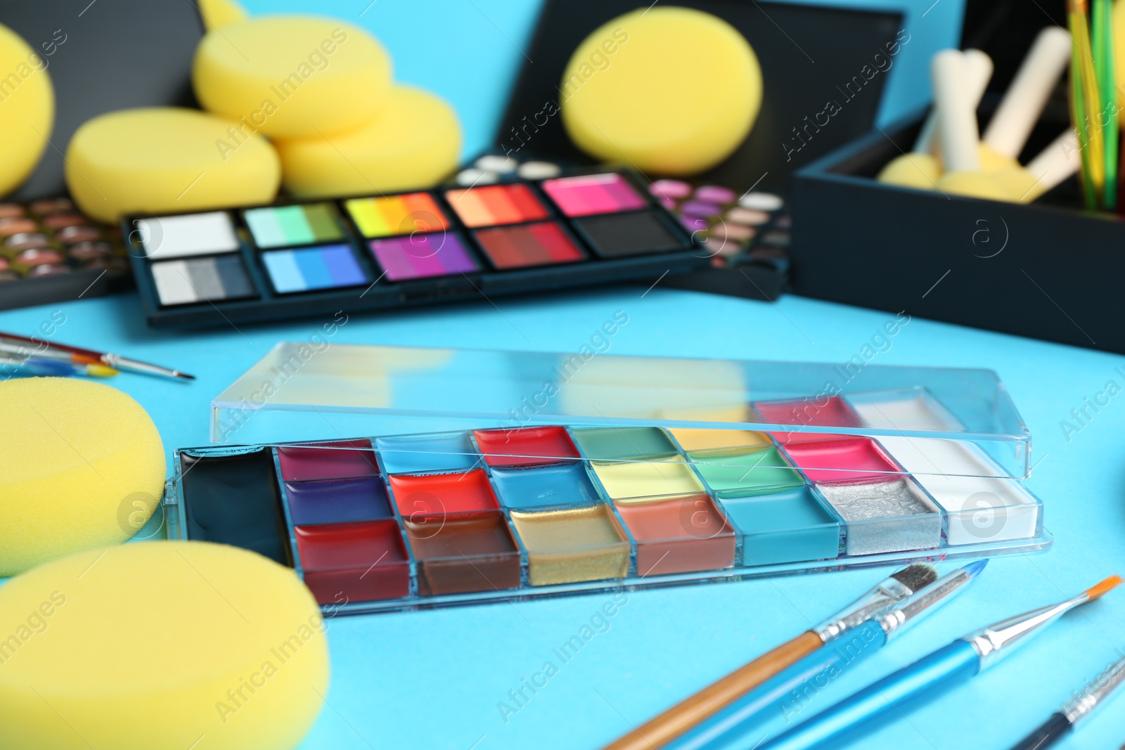 Photo of Bright face paints, brushes and sponges on light blue background, closeup