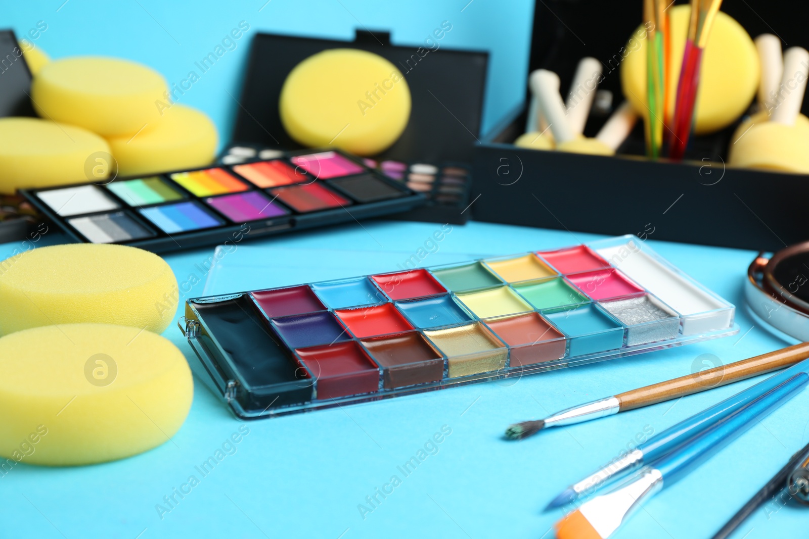 Photo of Bright face paints, brushes and sponges on light blue background, closeup